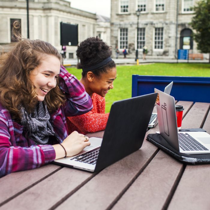 Smiling university students with laptops on table at campus